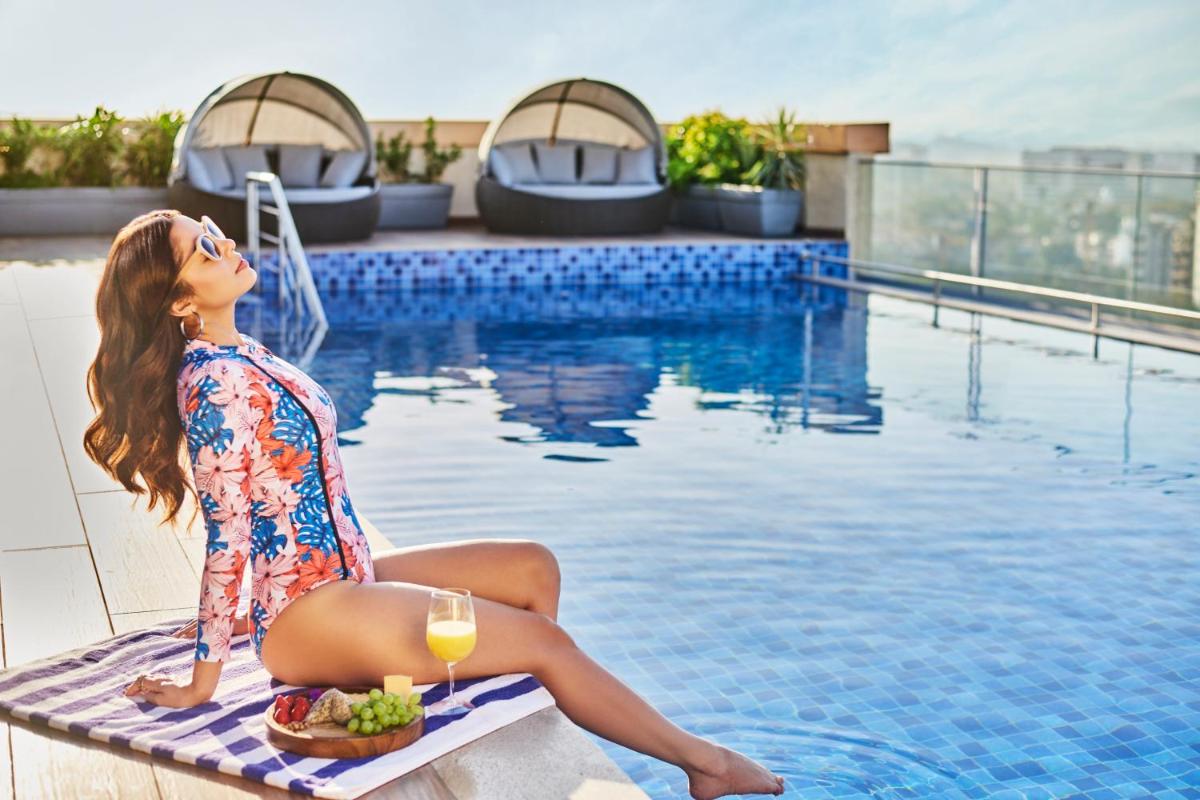 a woman sitting on a towel next to a swimming pool with a plate of food at Novotel Mumbai International Airport in Mumbai