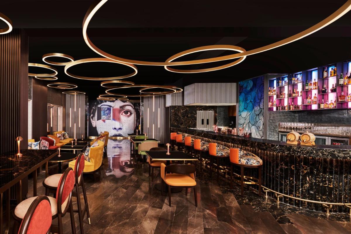 a restaurant with a bar with orange chairs and a chandelier at Novotel Mumbai International Airport in Mumbai