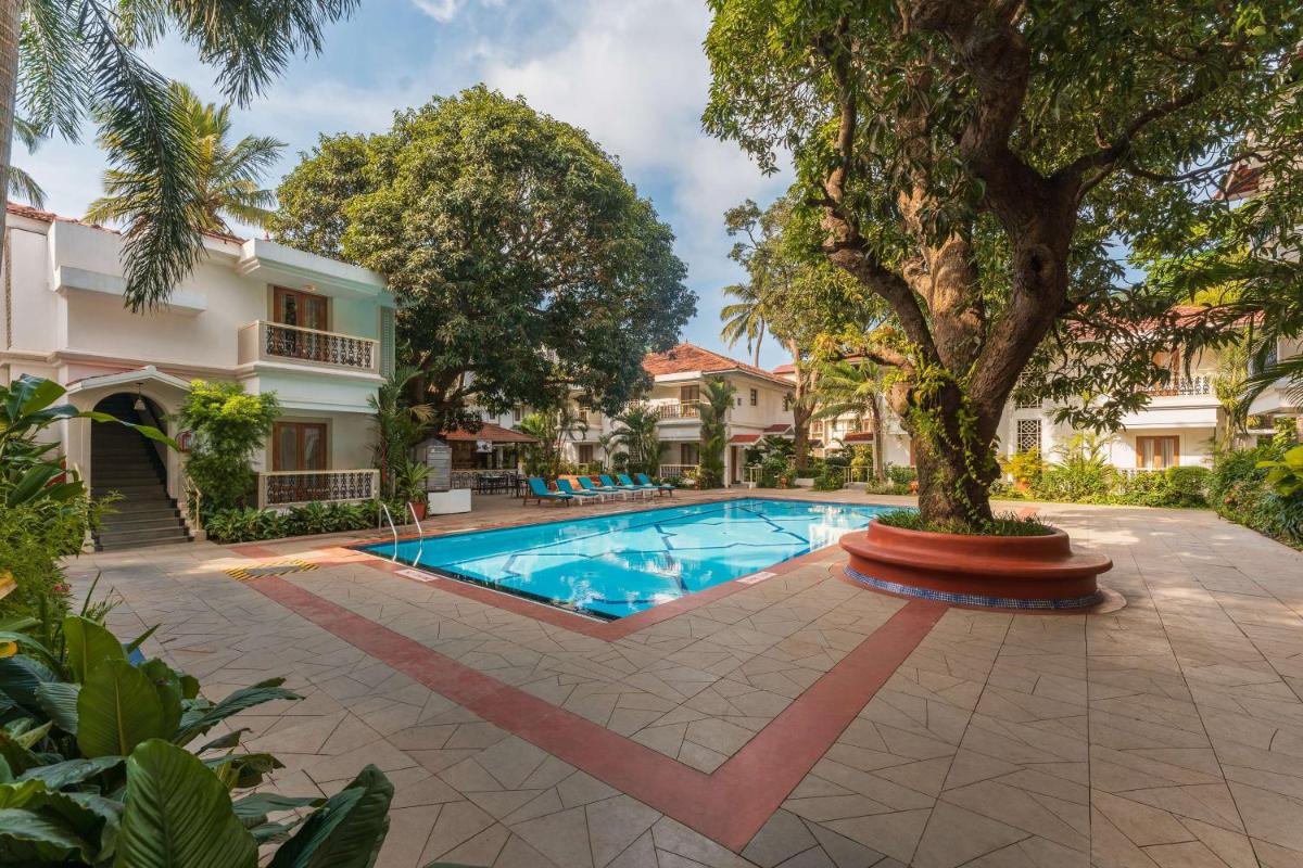 a swimming pool with a tree in front of a house at Radisson Goa Candolim in Candolim