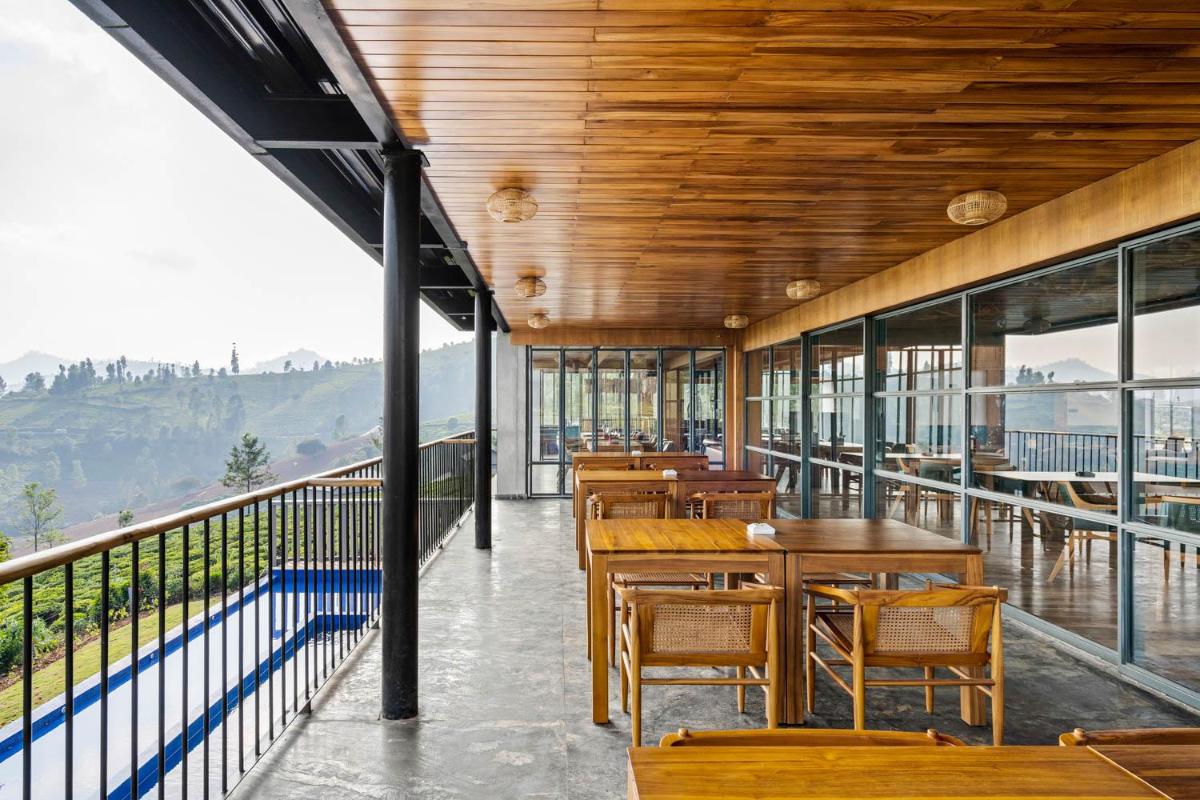 a restaurant with wooden tables and chairs on a balcony at WelcomHeritage Ayatana Ooty in Ooty