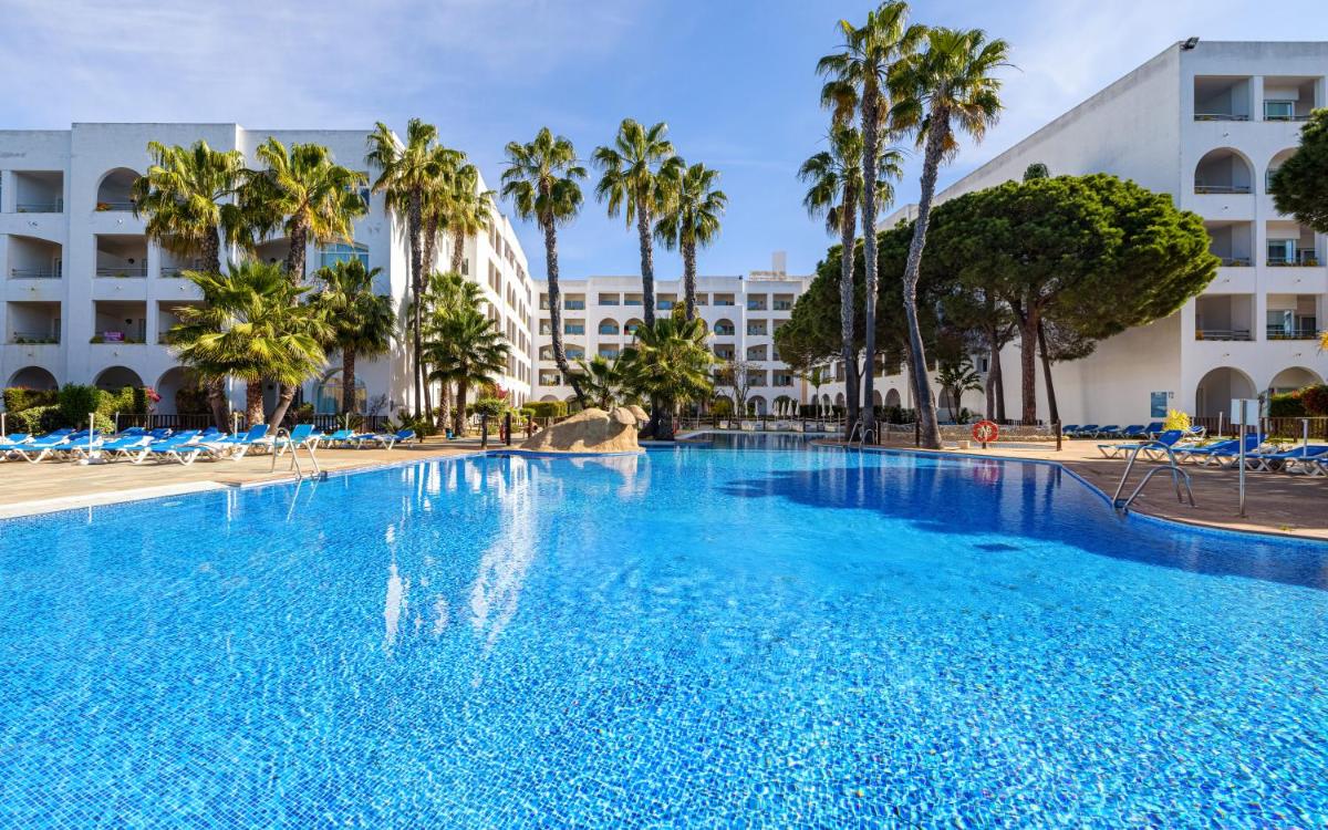 Una gran piscina con palmeras y un edificio. en Playacartaya, en El Portil