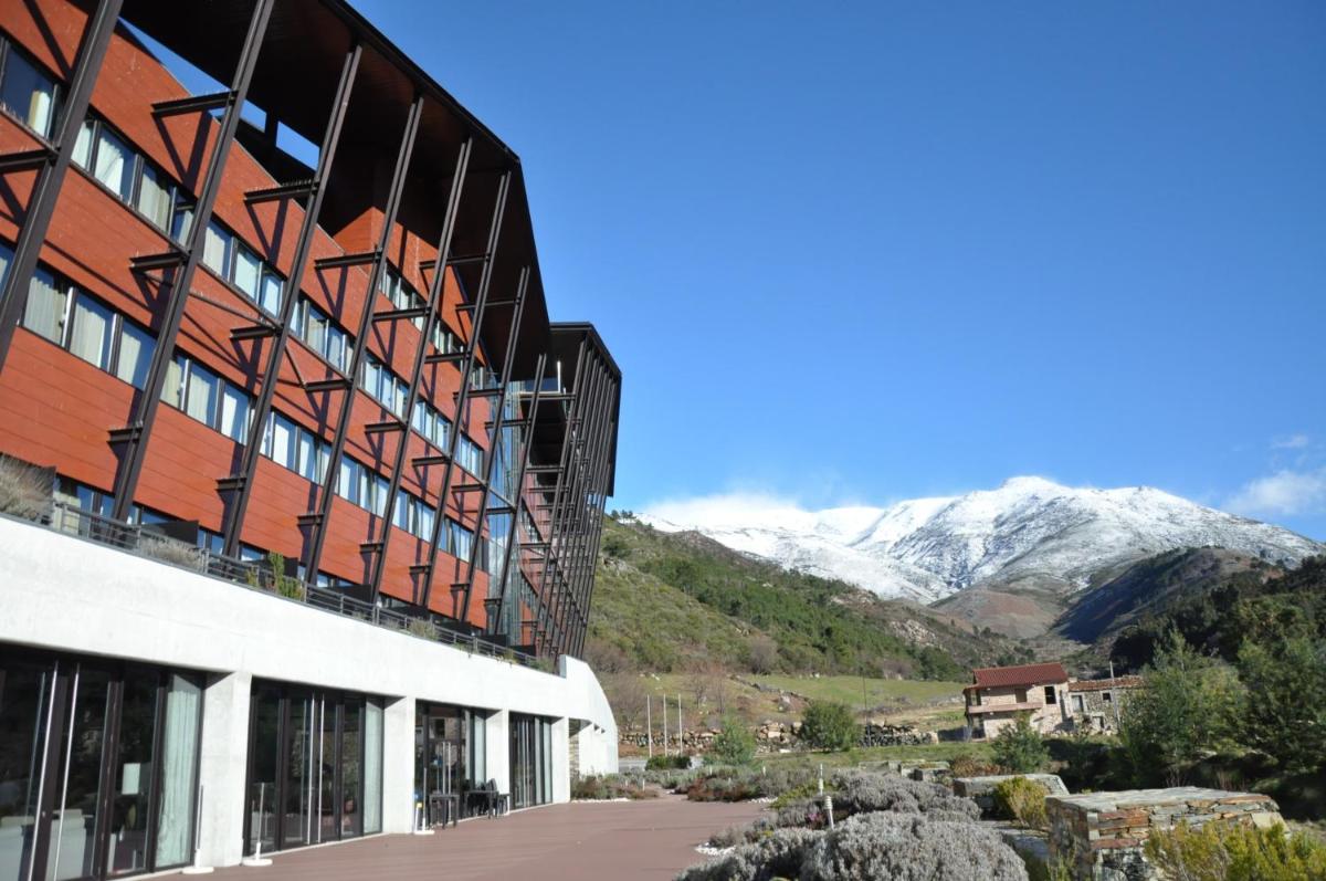 um edifício com montanhas cobertas de neve ao fundo em H2otel Congress & Medical SPA em Unhais da Serra