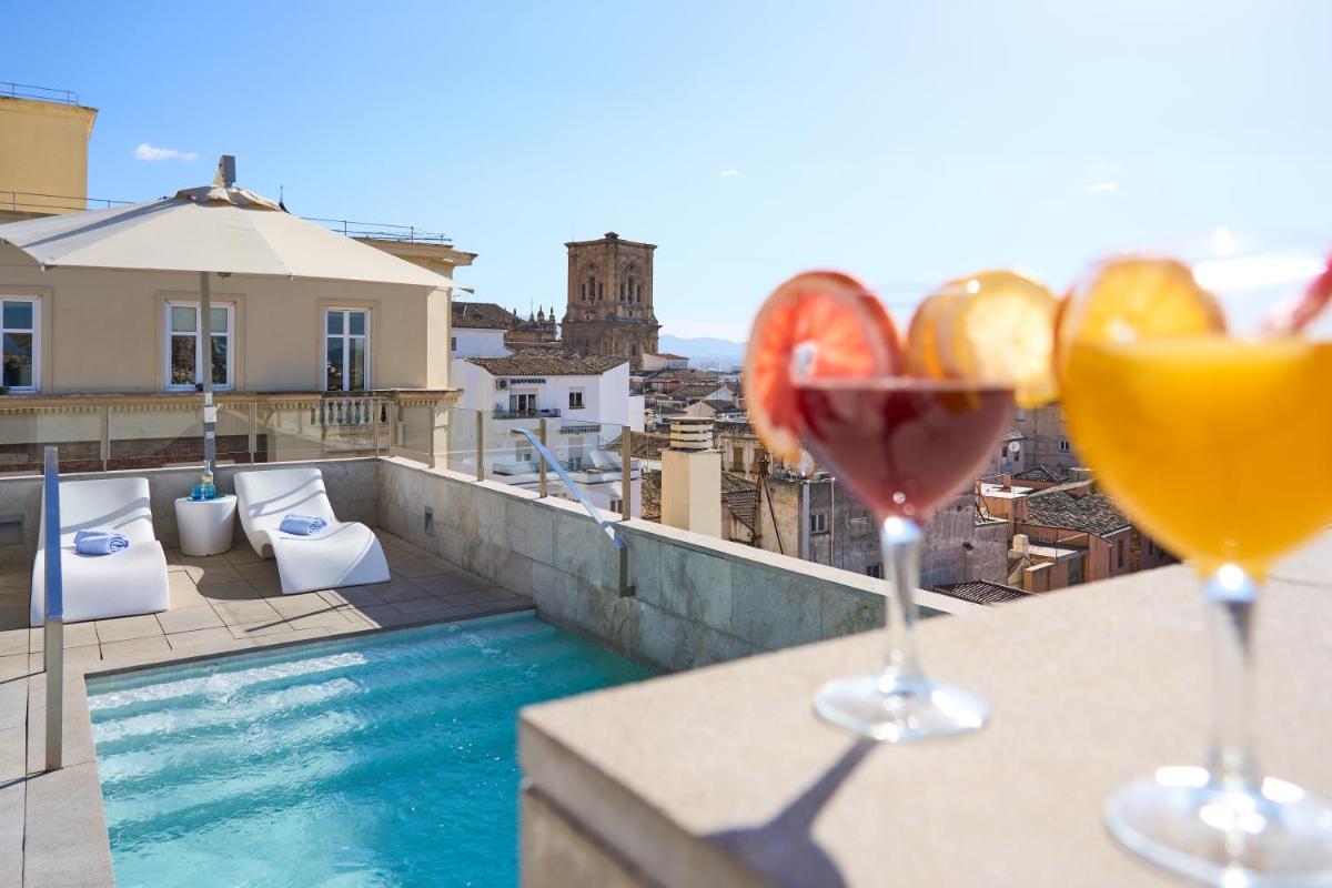 2 copas de vino en un balcón con piscina en Hotel Maciá Granada Five Senses Rooms & Suites, en Granada