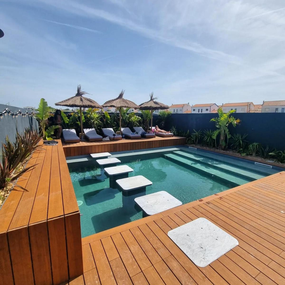 uma piscina com cadeiras e um deque de madeira em The Salty Pelican Yoga & Surf Retreat em Peniche