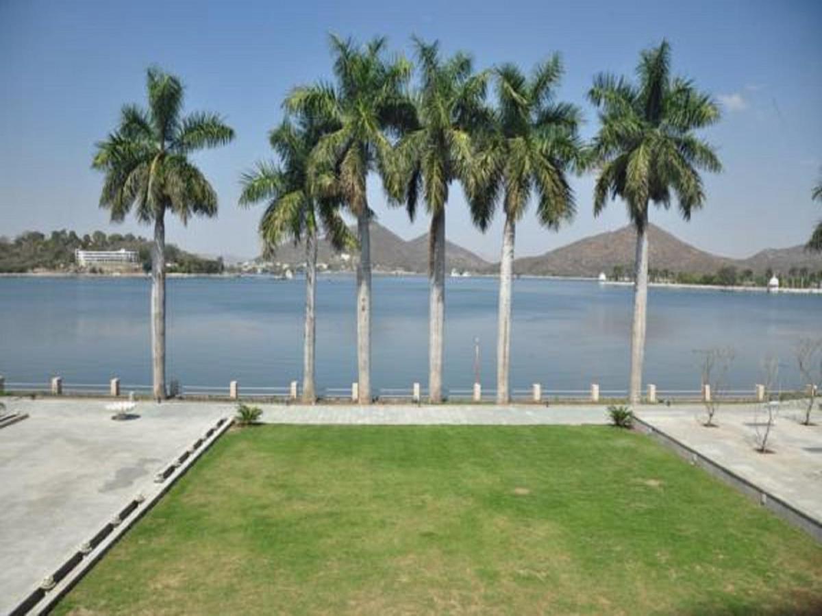a row of palm trees next to a body of water at Hotel Lakend in Udaipur