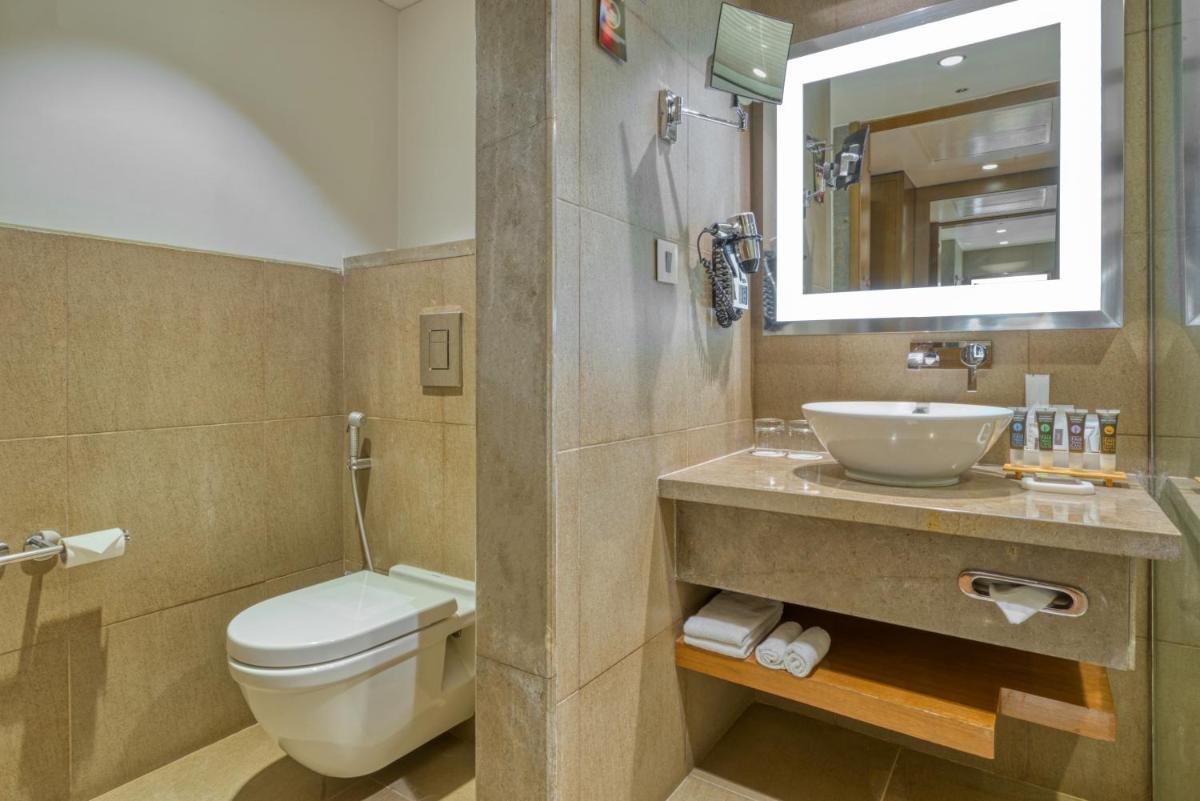 a bathroom with a toilet and a sink and a mirror at Novotel Bengaluru Outer Ring Road in Bengaluru