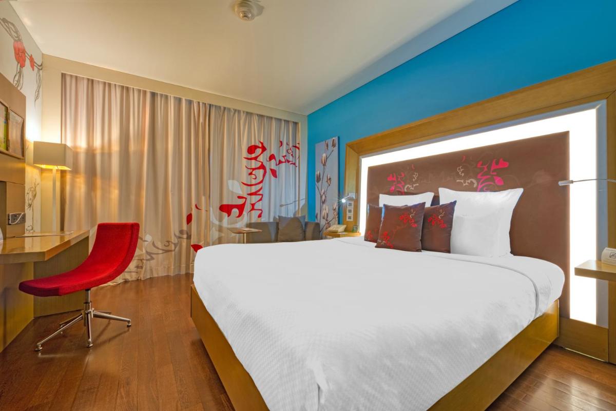 a bedroom with a large bed and a red chair at Novotel Bengaluru Outer Ring Road in Bengaluru
