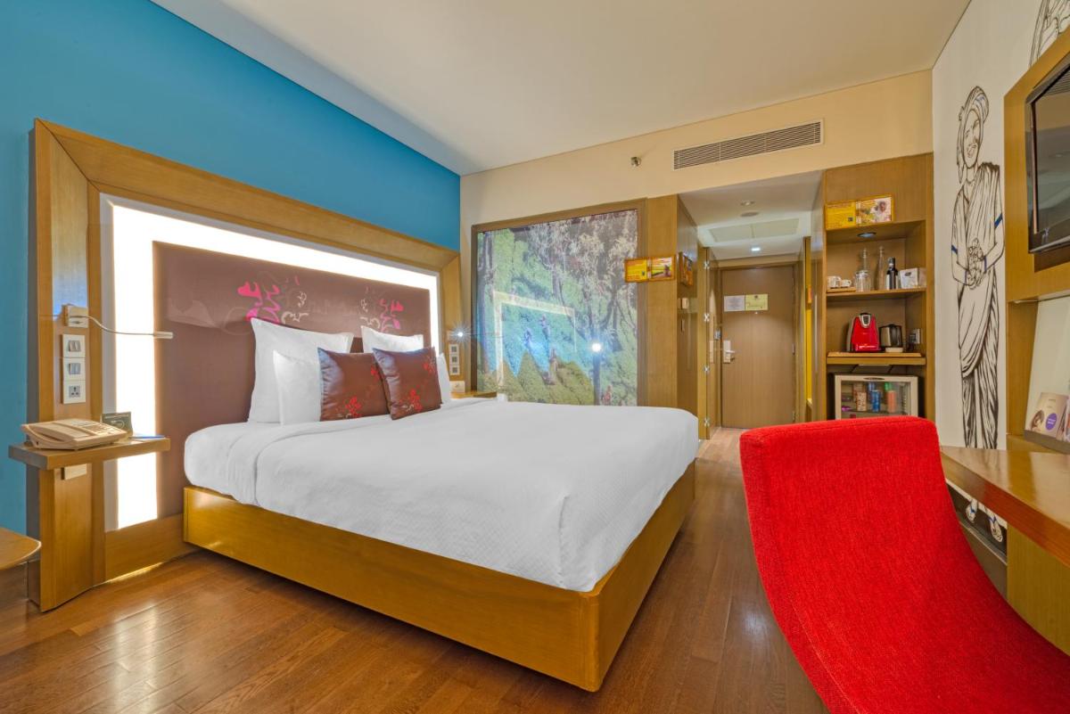 a bedroom with a large bed and a red chair at Novotel Bengaluru Outer Ring Road in Bengaluru