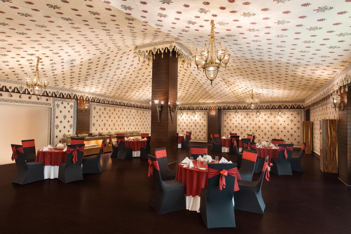 a dining room with tables and chairs and a chandelier at Radisson Jaipur City Center in Jaipur