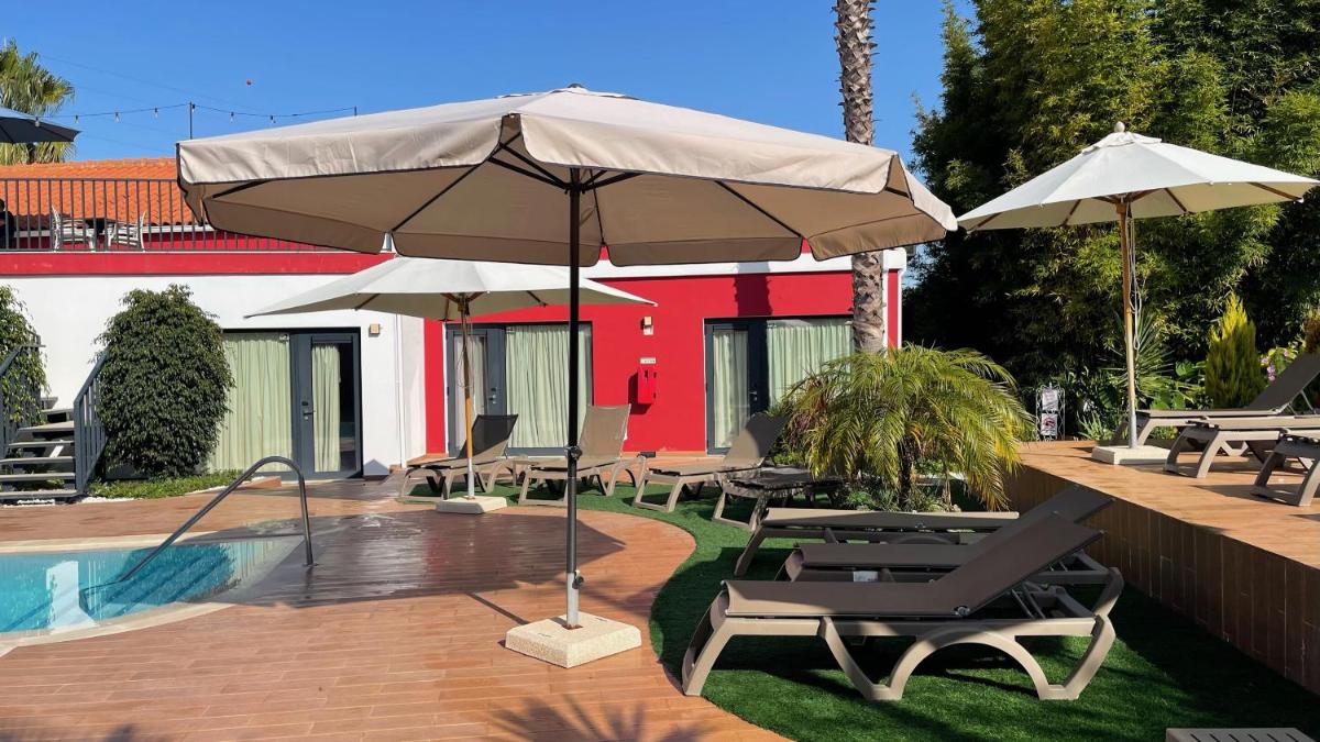 um pátio com cadeiras e guarda-sóis ao lado de uma piscina em Villa 3 Caparica - Lisbon Gay Beach Resort em Charneca