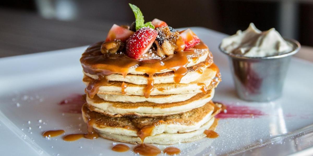 a stack of pancakes with strawberries and syrup on a plate at Crowne Plaza Ahmedabad City Centre by IHG in Ahmedabad