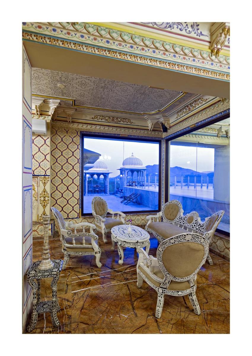 a living room with chairs and tables and a large window at Chunda Palace in Udaipur