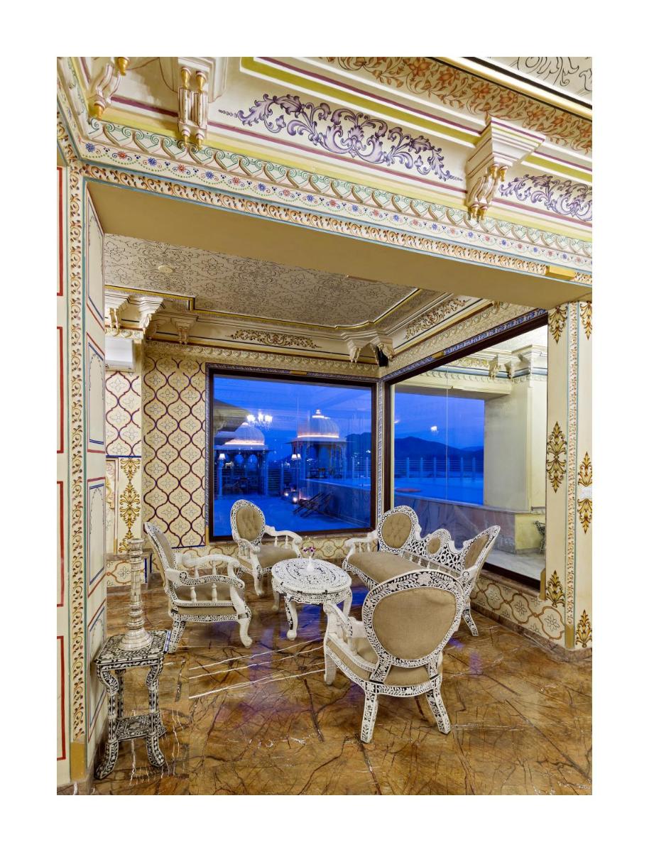 a living room with chairs and tables and a large window at Chunda Palace in Udaipur