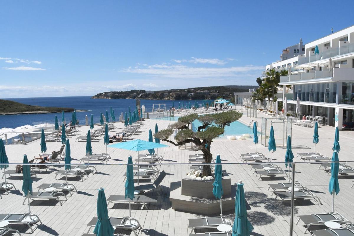 una playa con sillas y sombrillas azules y un edificio en Elba Sunset Mallorca Thalasso Spa, en Palmanova