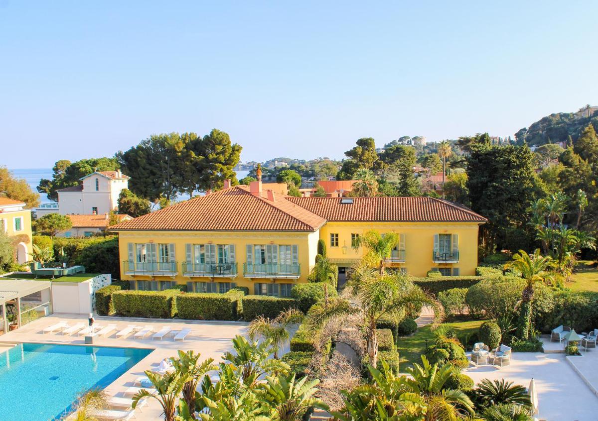 une grande maison jaune avec une piscine et des palmiers dans l'établissement Hotel Royal-Riviera, à Saint-Jean-Cap-Ferrat