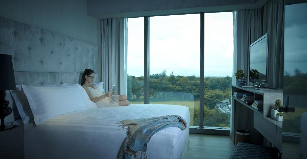 a woman sitting on a bed looking at her cell phone at Pan Pacific Serviced Suites Beach Road, Singapore in Singapore