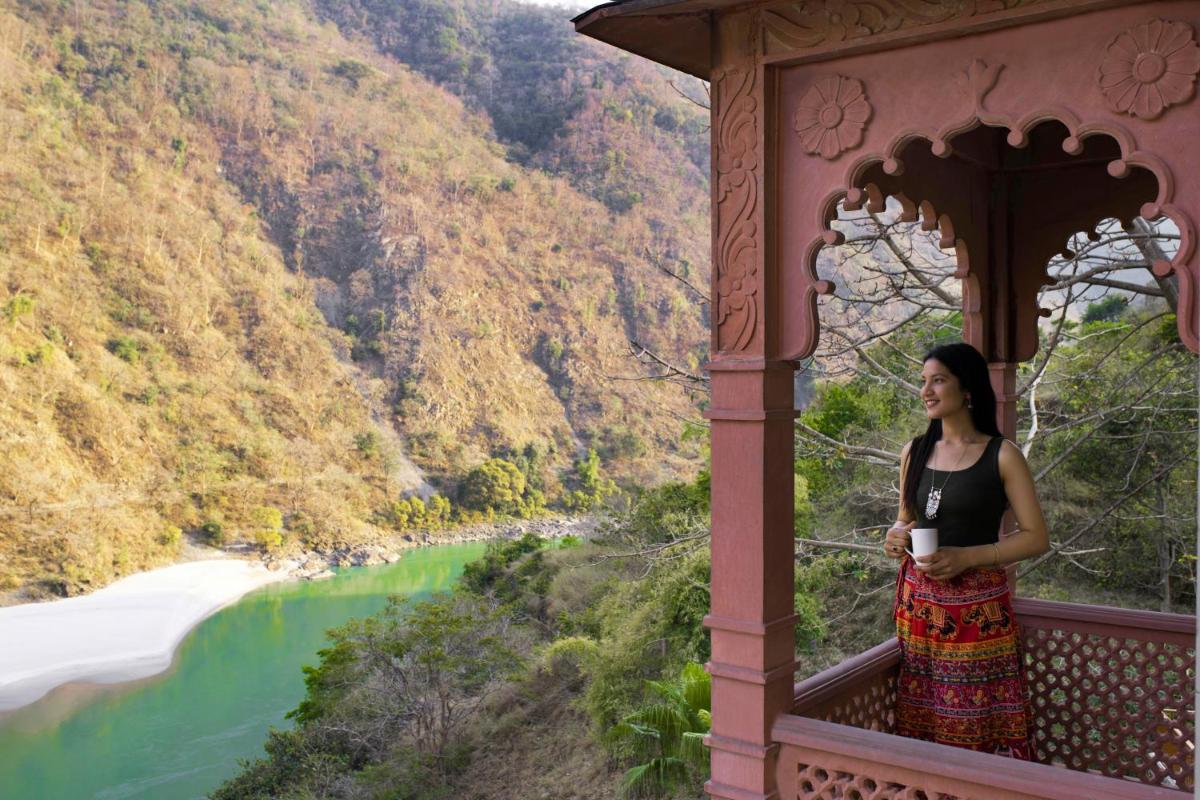 a woman standing on a balcony with a cup of coffee at Raga on the Ganges, Rishikesh in Rishīkesh