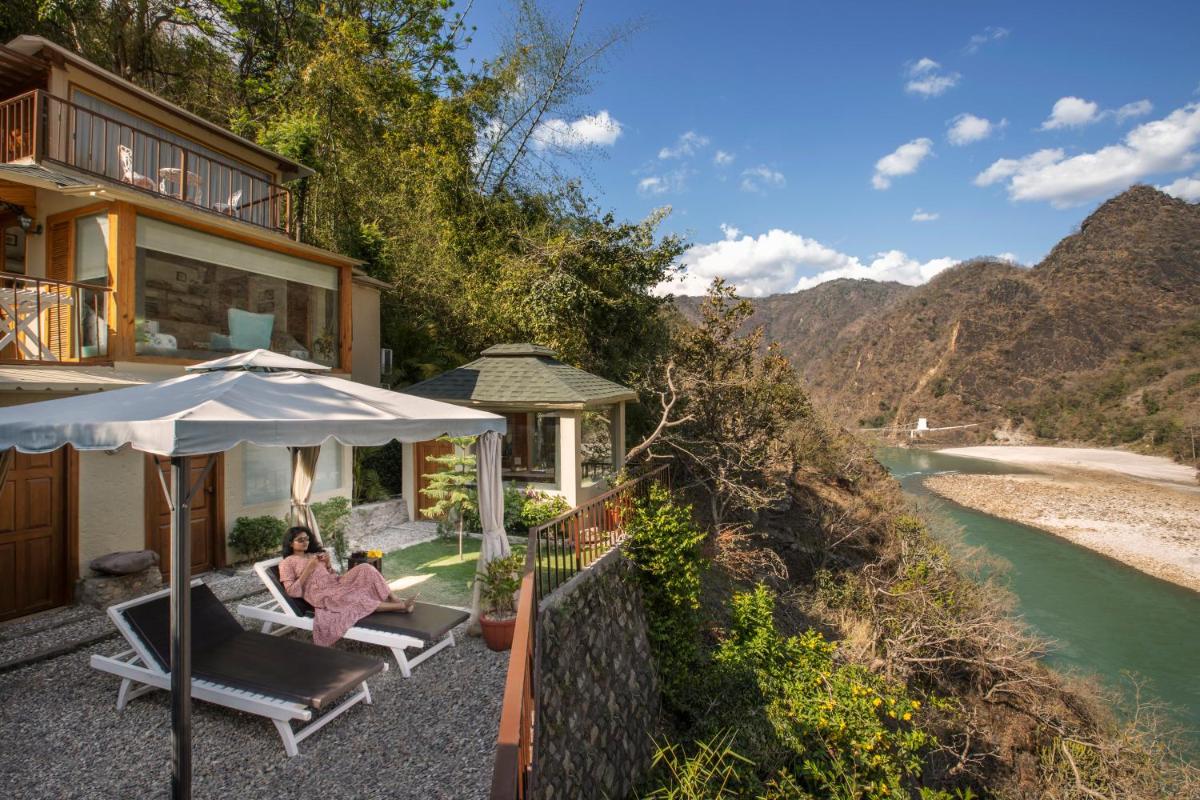 a woman sitting on a chair next to a house next to a river at Raga on the Ganges, Rishikesh in Rishīkesh
