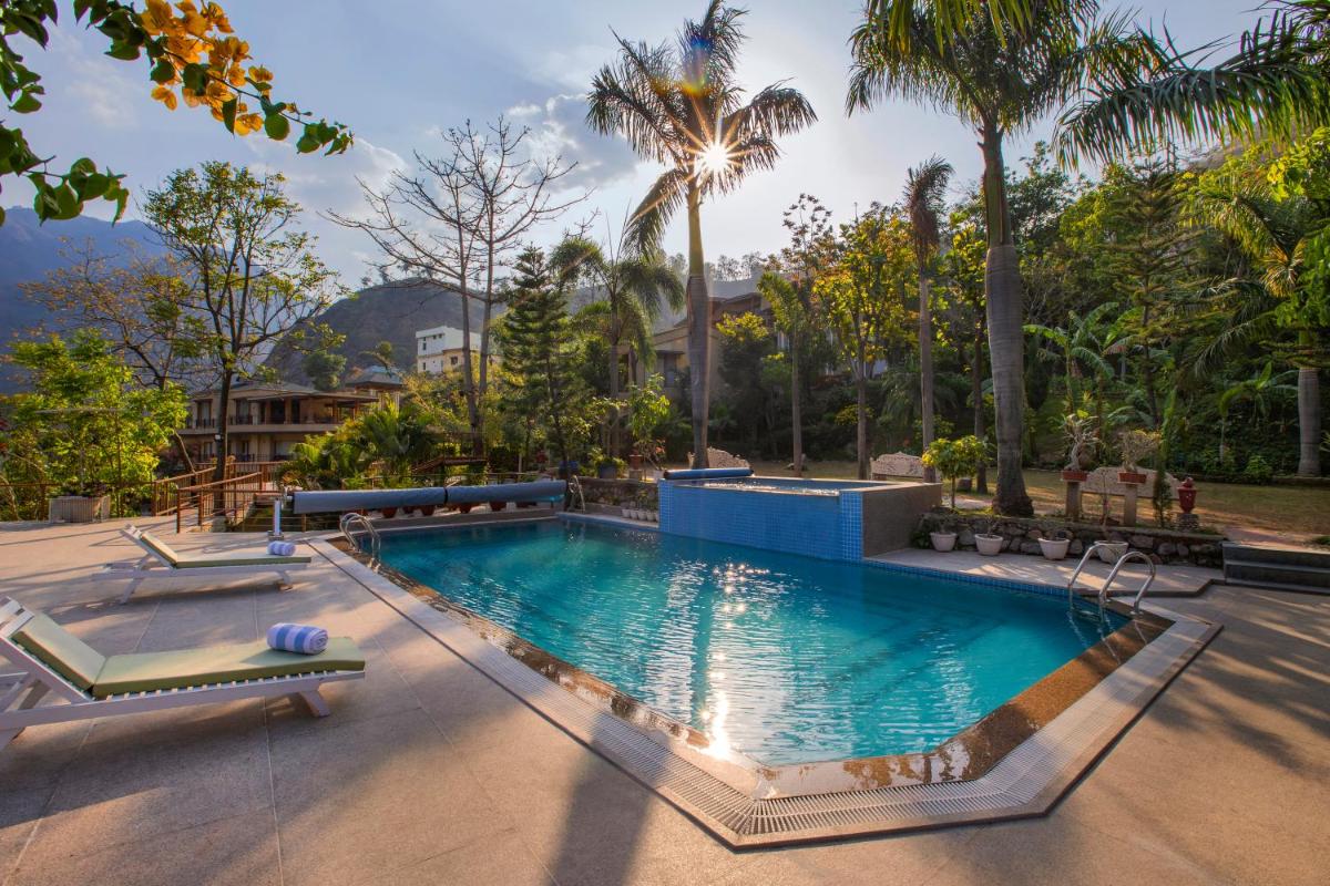 a pool with two lounge chairs and palm trees at Raga on the Ganges, Rishikesh in Rishīkesh