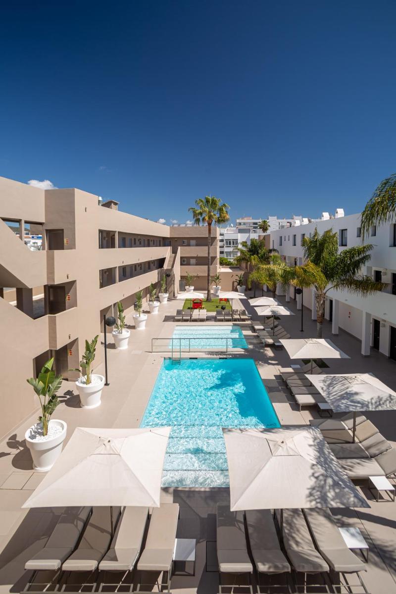 Una imagen de una piscina de hotel con sillas y sombrillas. en Migjorn Ibiza Suites & Spa, en Playa d'en Bossa