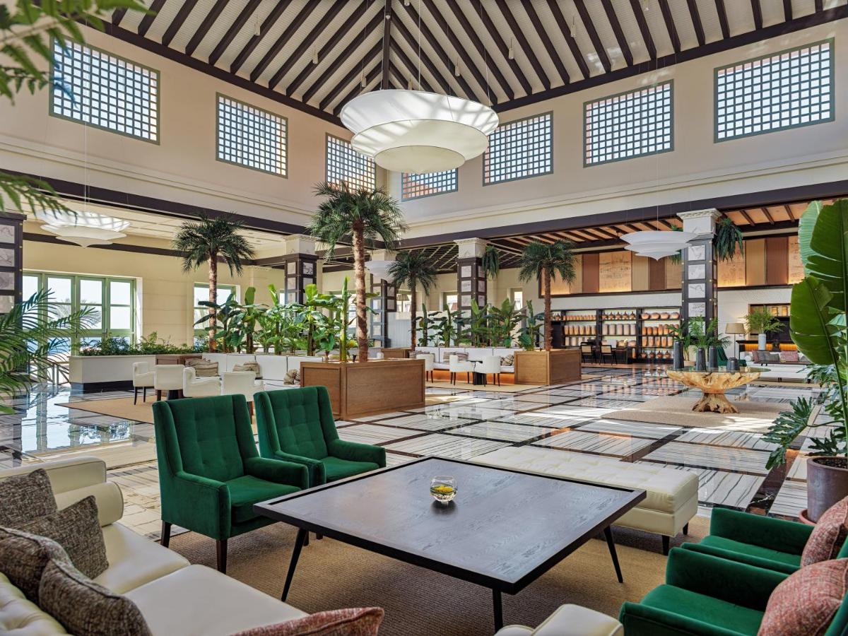 Un gran vestíbulo con sillas verdes y una mesa. en H10 Costa Adeje Palace, en Adeje