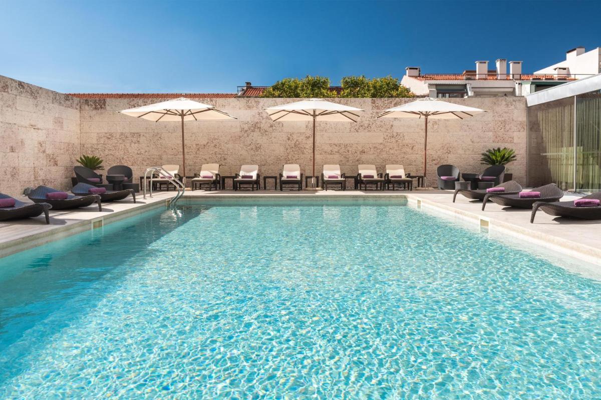 uma piscina com cadeiras e guarda-sóis em um prédio em Sheraton Lisboa Hotel & Spa em Lisboa