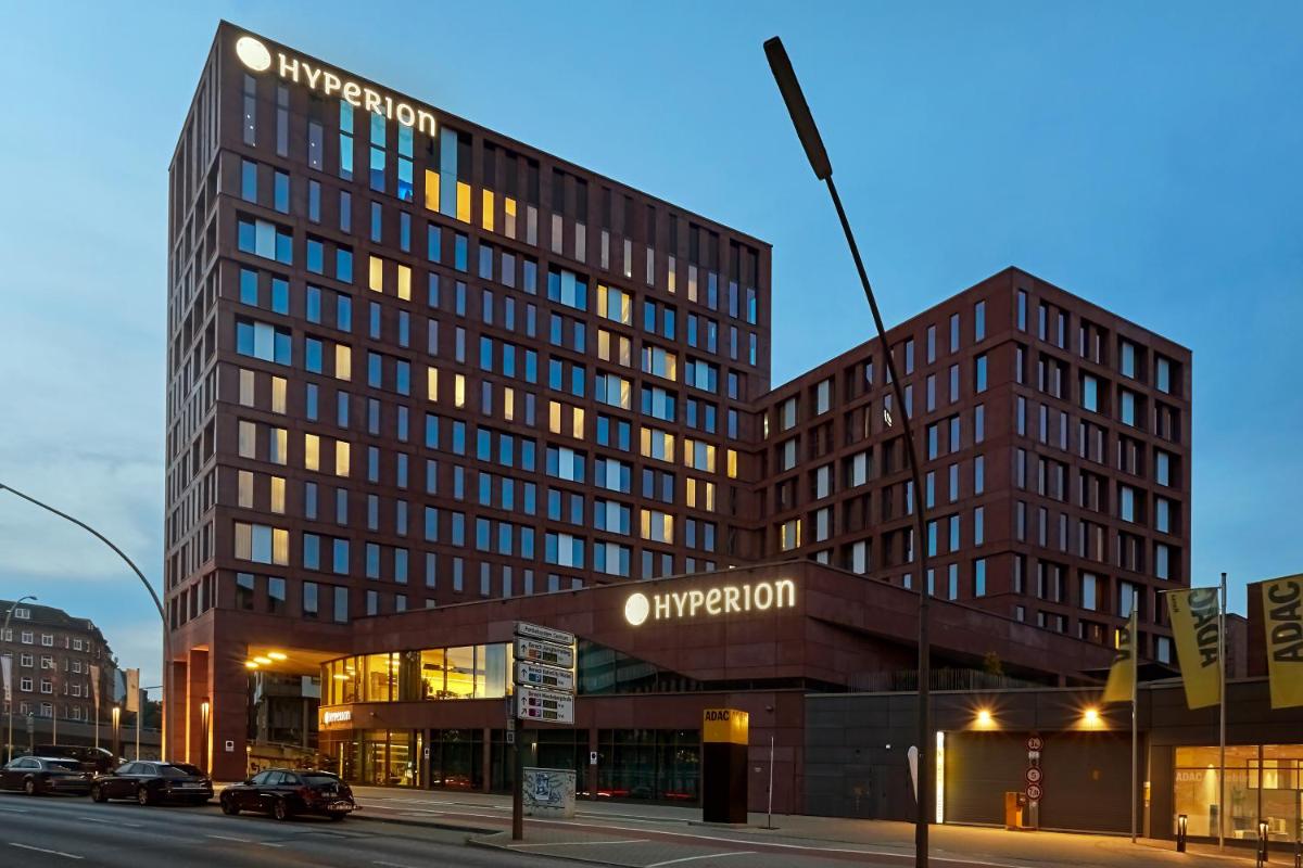 ein hohes Gebäude in einer Stadtstraße mit einem Gebäude in der Unterkunft HYPERION Hotel Hamburg in Hamburg ein hohes Gebäude in einer Stadtstraße mit einem Gebäude in der Unterkunft HYPERION Hotel Hamburg in Hamburg