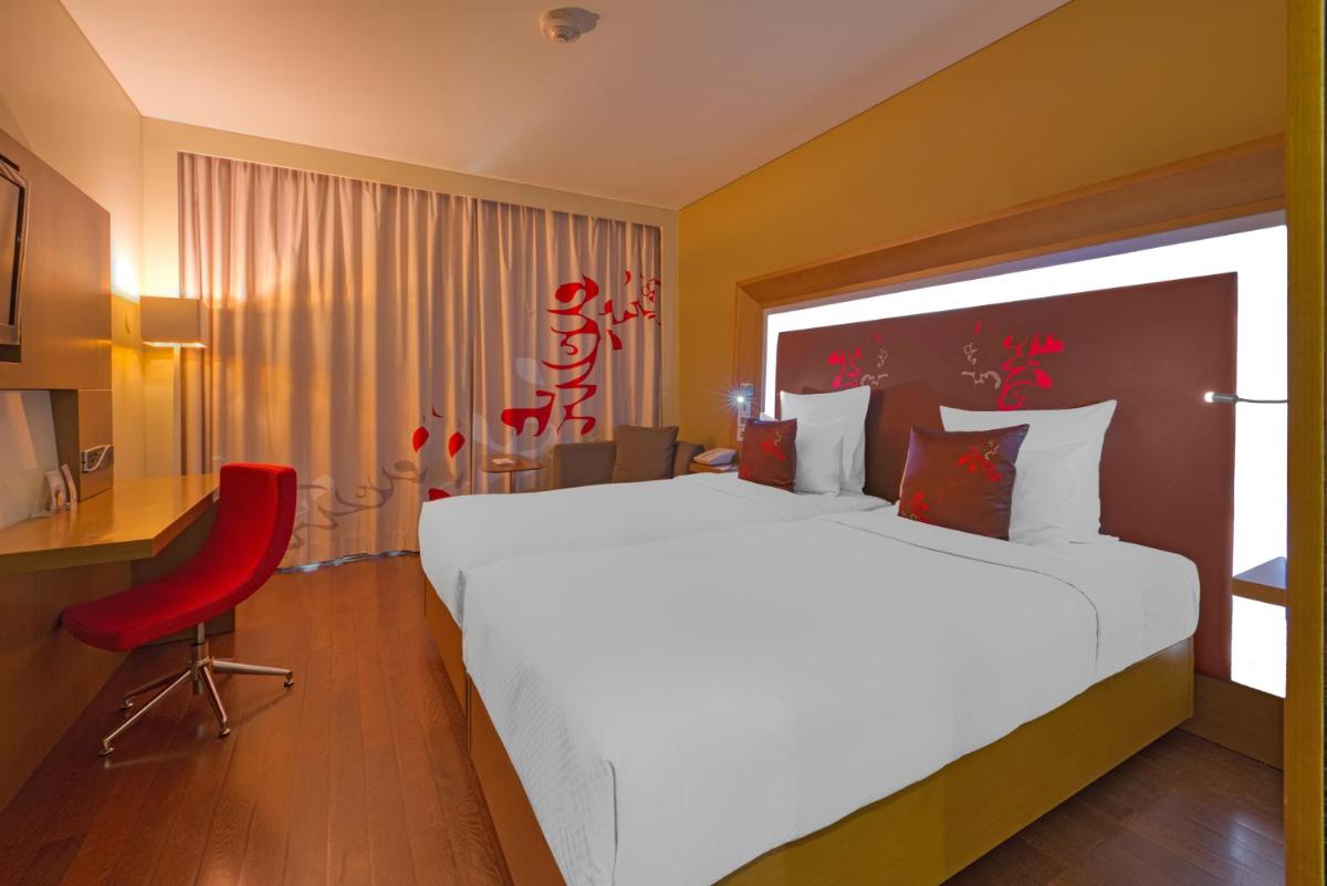 a bedroom with a large bed and a red chair at Novotel Bengaluru Outer Ring Road in Bengaluru
