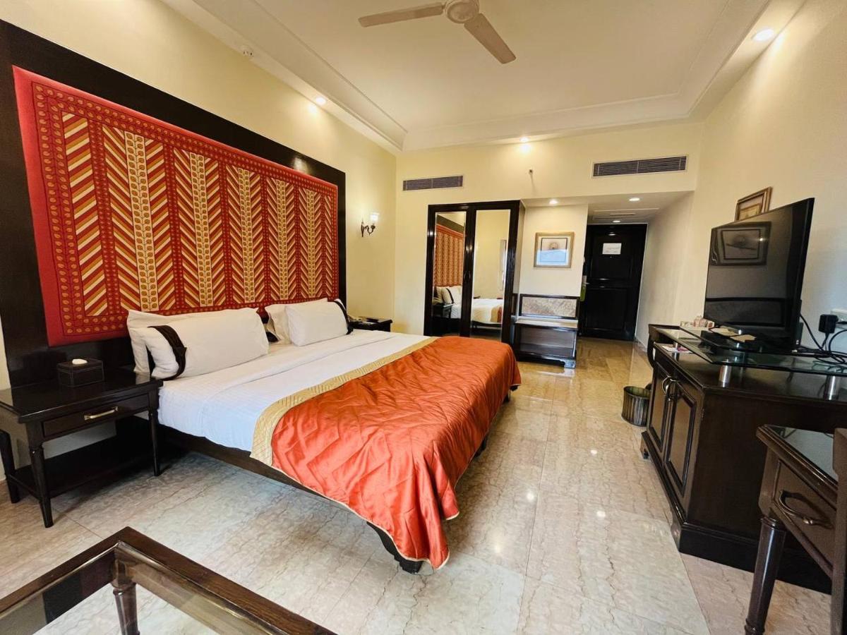 a bedroom with a large bed and a flat screen tv at The Lalit Laxmi Vilas Palace in Udaipur