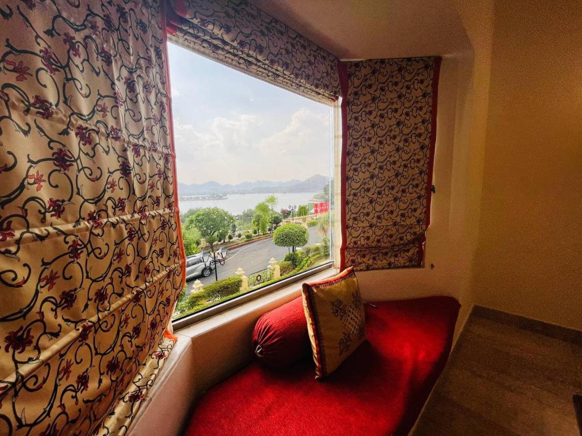a window with a red couch in front of a red pillow at The Lalit Laxmi Vilas Palace in Udaipur