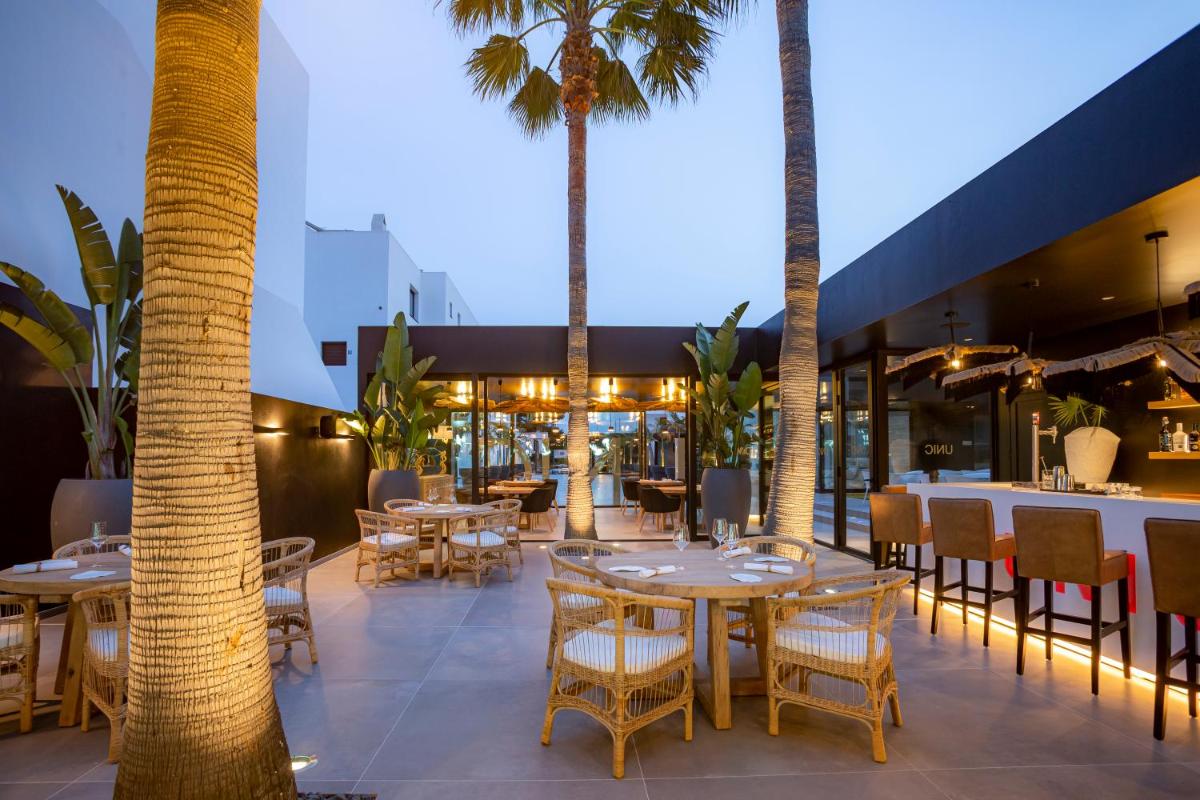 Un restaurante con mesas y sillas y palmeras. en Migjorn Ibiza Suites & Spa, en Playa d'en Bossa