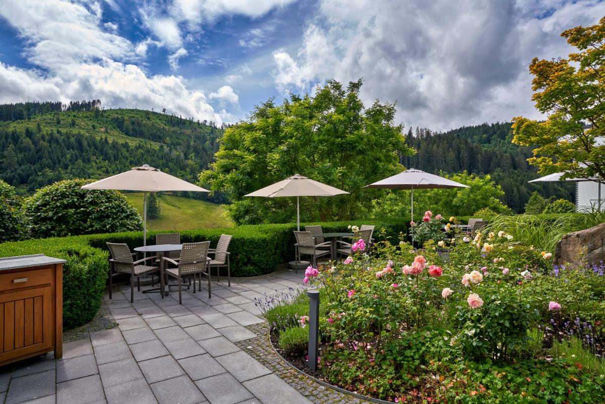 eine Terrasse mit Tischen und Sonnenschirmen in einem Garten in der Unterkunft Hotel Traube Tonbach in Baiersbronn