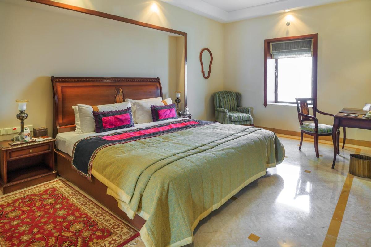 a bedroom with a large bed and a desk at The Lalit Laxmi Vilas Palace in Udaipur