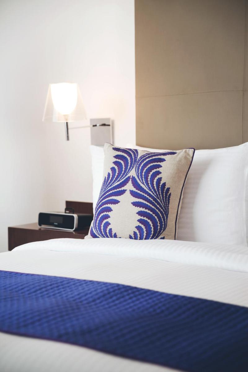 a bed with a blue and white pillow and a lamp at The Anya Hotel-Golf Course Road in Gurgaon