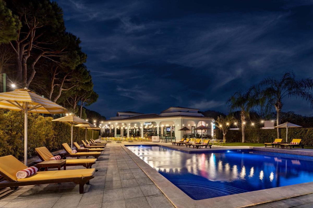 uma piscina à noite com cadeiras e guarda-sóis em The Magnolia Hotel na Quinta do Lago