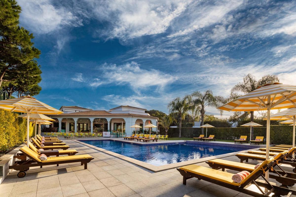 uma piscina com espreguiçadeiras e guarda-sóis em The Magnolia Hotel na Quinta do Lago