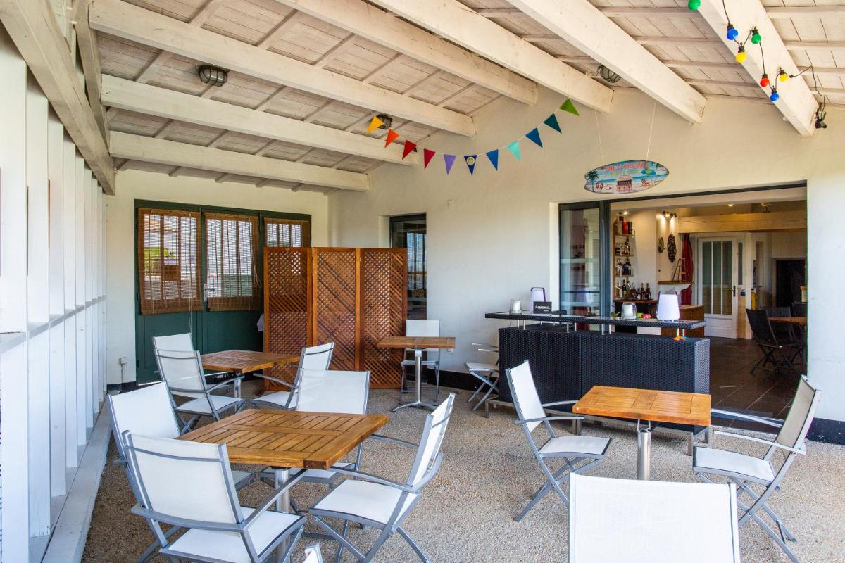 d'une terrasse avec des tables en bois et des chaises blanches. dans l'établissement Hôtel Les Vignes de la Chapelle, "The Originals Relais", à Sainte-Marie de Ré