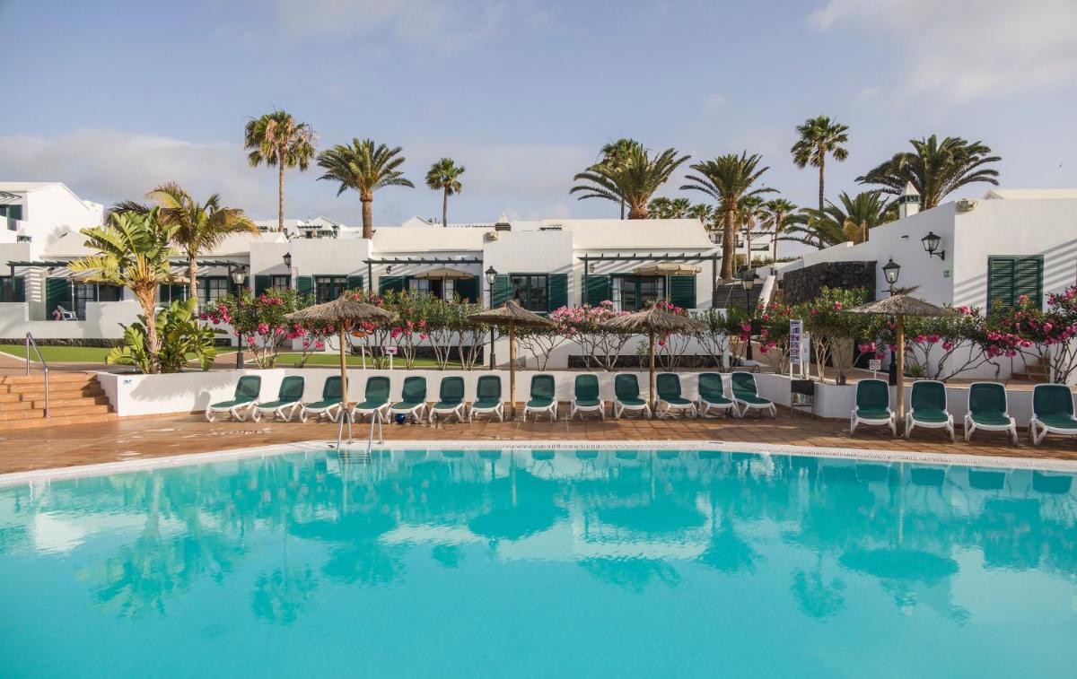 Una piscina con sillas y sombrillas frente a un resort. en ILUNION Costa Sal Lanzarote, en Puerto del Carmen