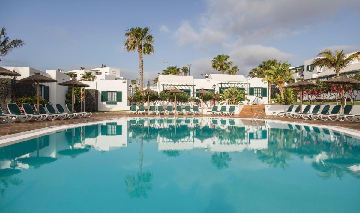 Una piscina en un resort con sillas y palmeras. en ILUNION Costa Sal Lanzarote, en Puerto del Carmen