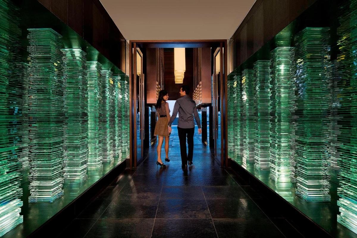 a man and woman walking through a hallway with green glass walls at JW Marriott Pune in Pune