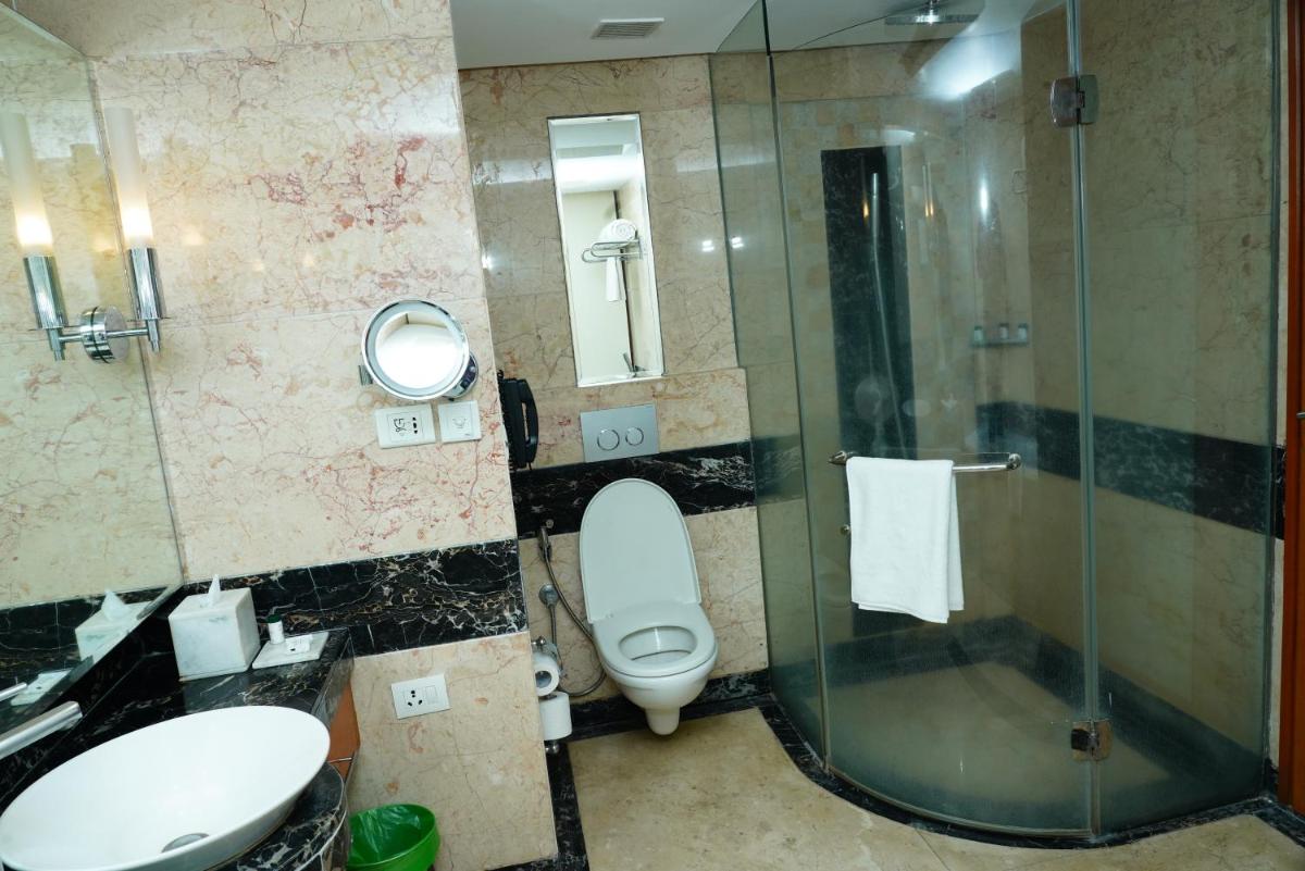 a bathroom with a toilet and a glass shower at Gokulam Grand Hotel & Spa Bangalore in Bengaluru a bathroom with a toilet and a glass shower at Gokulam Grand Hotel & Spa Bangalore in Bengaluru