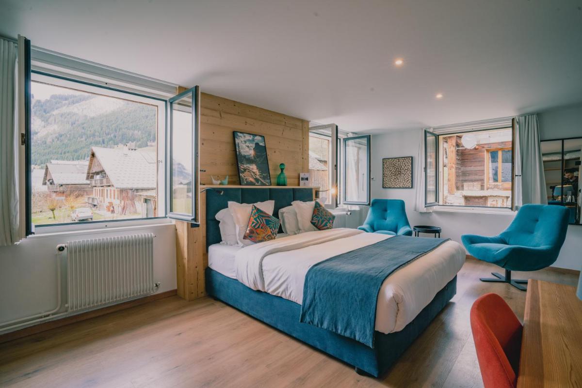 une chambre avec un grand lit et deux chaises bleues dans l'établissement Terra-Beka Lodge, à La Chapelle-dʼAbondance