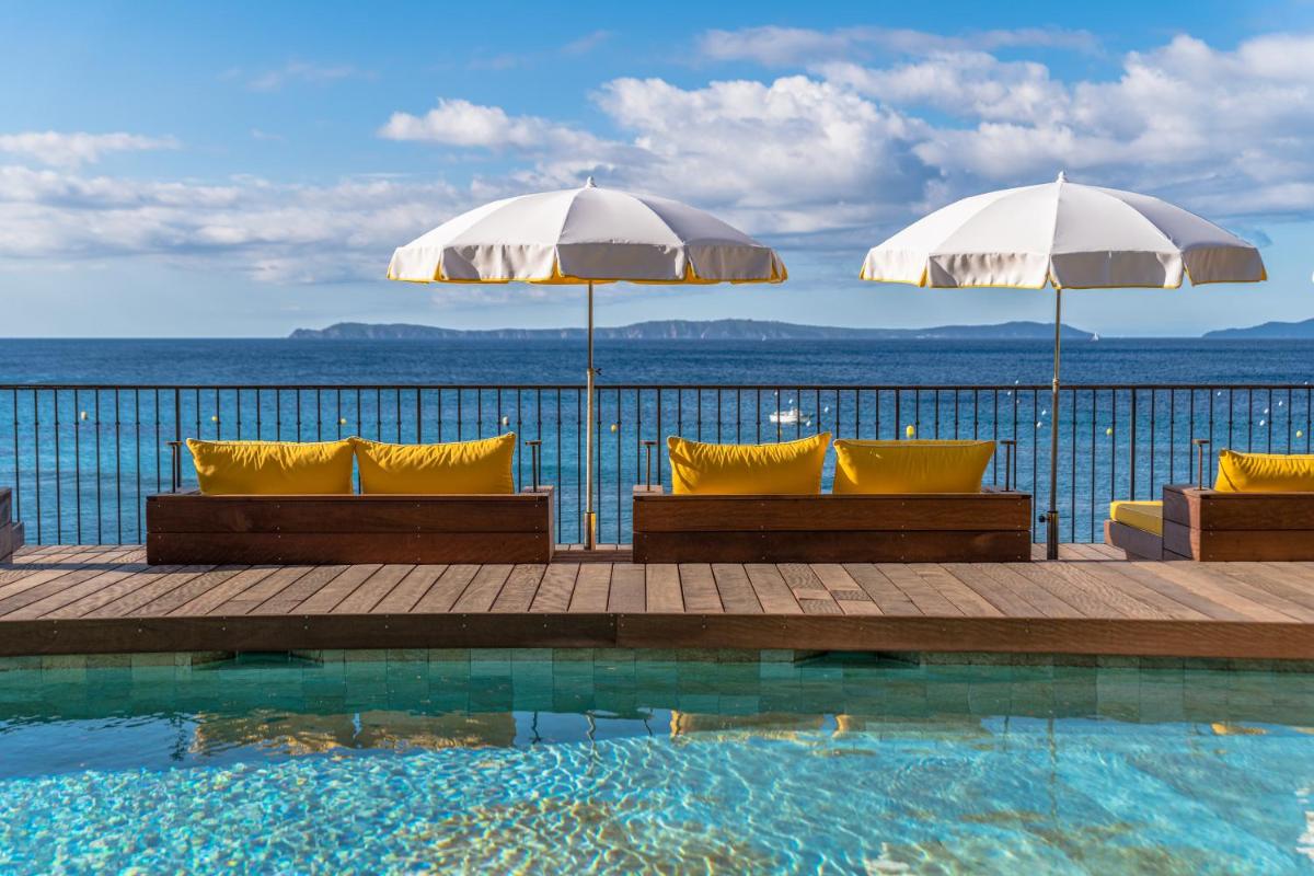 - une piscine avec deux parasols et des chaises à côté de l'océan dans l'établissement Hôtel Le Bailli De Suffren, à Rayol-Canadel-sur-Mer 121 autres photos