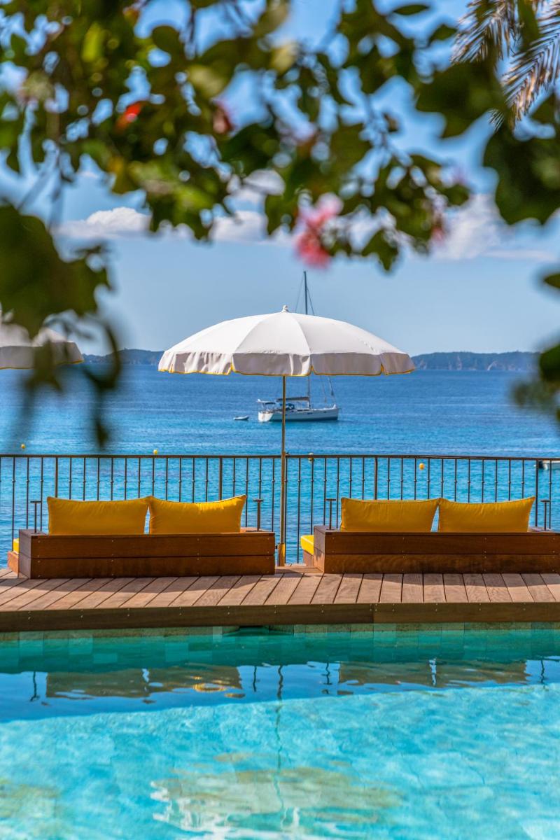 une piscine avec deux chaises et un parasol dans l'établissement Hôtel Le Bailli De Suffren, à Rayol-Canadel-sur-Mer