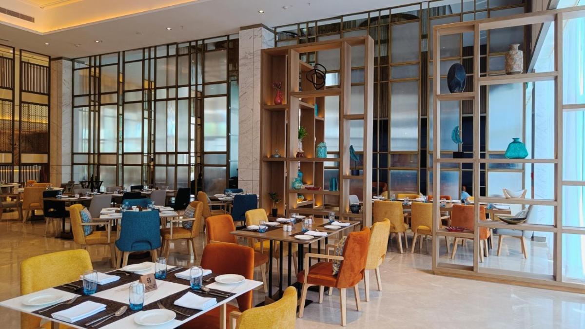 a restaurant with tables and chairs and windows at Holiday Inn Lucknow Airport by IHG in Lucknow