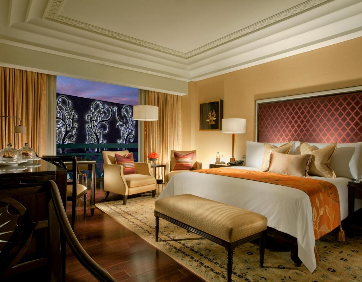 a bedroom with a large bed and a desk and chairs at The Leela Palace Chennai in Chennai a bedroom with a large bed and a desk and chairs at The Leela Palace Chennai in Chennai