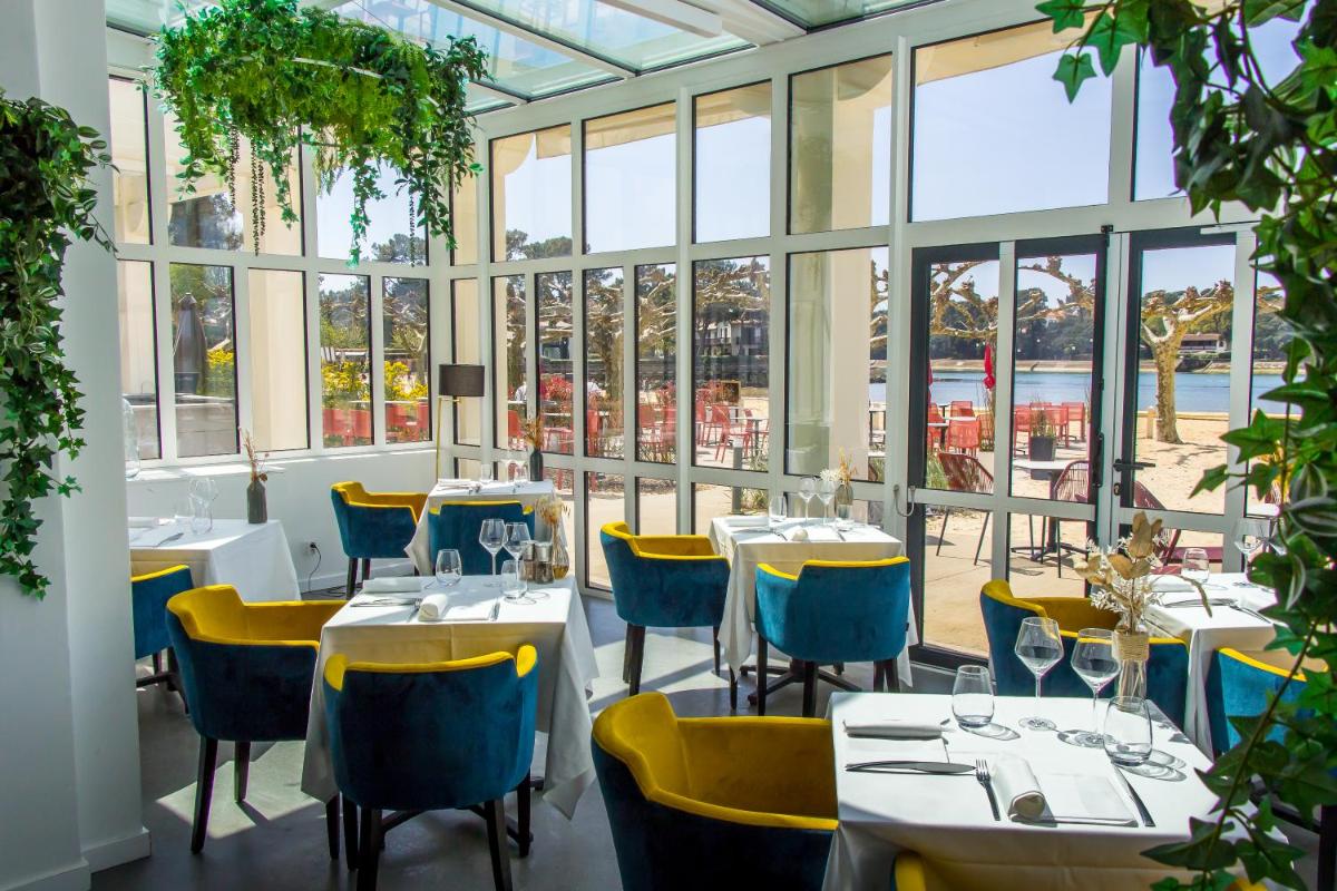 un restaurant avec des tables et des chaises dans une salle avec des fenêtres dans l'établissement Hôtel du Parc & Spa, à Hossegor 44 autres photos
