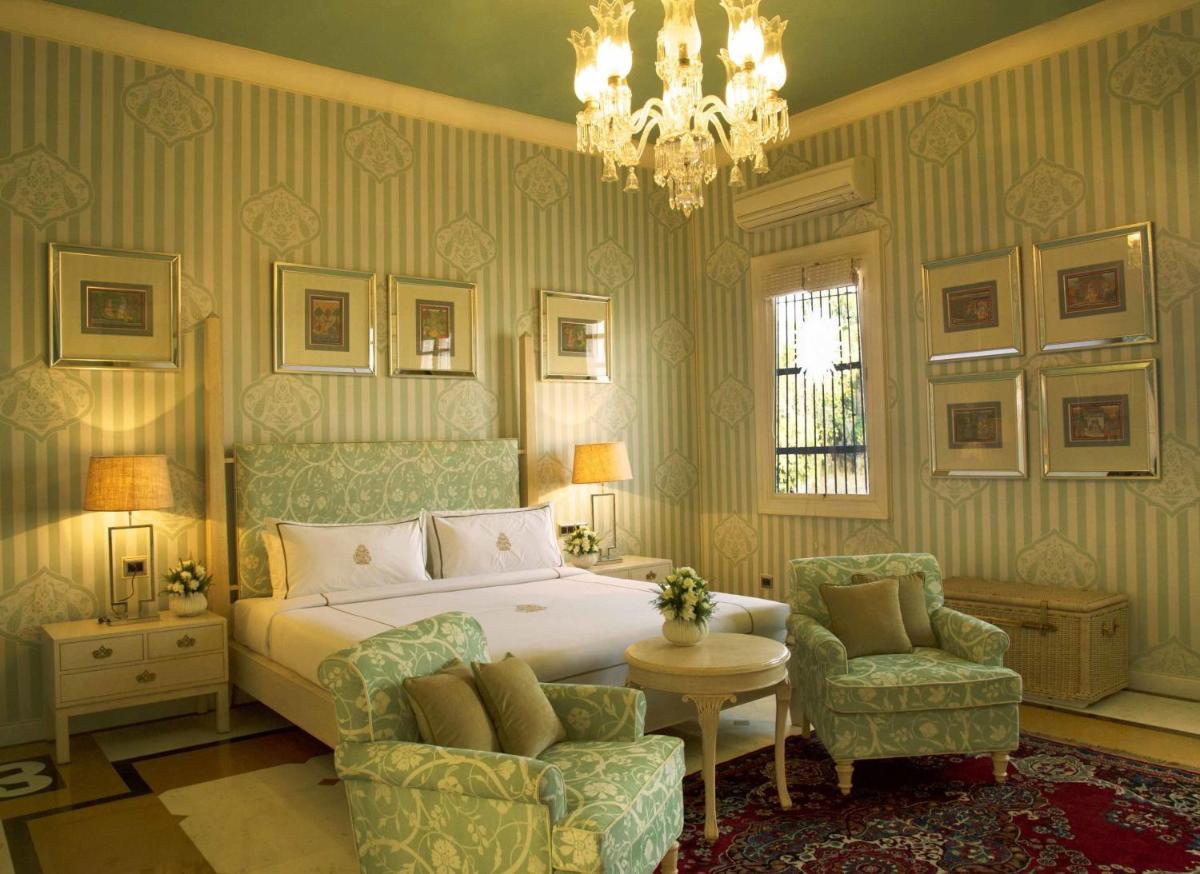 a bedroom with a bed and a chair and a chandelier at Rajmahal Palace RAAS in Jaipur