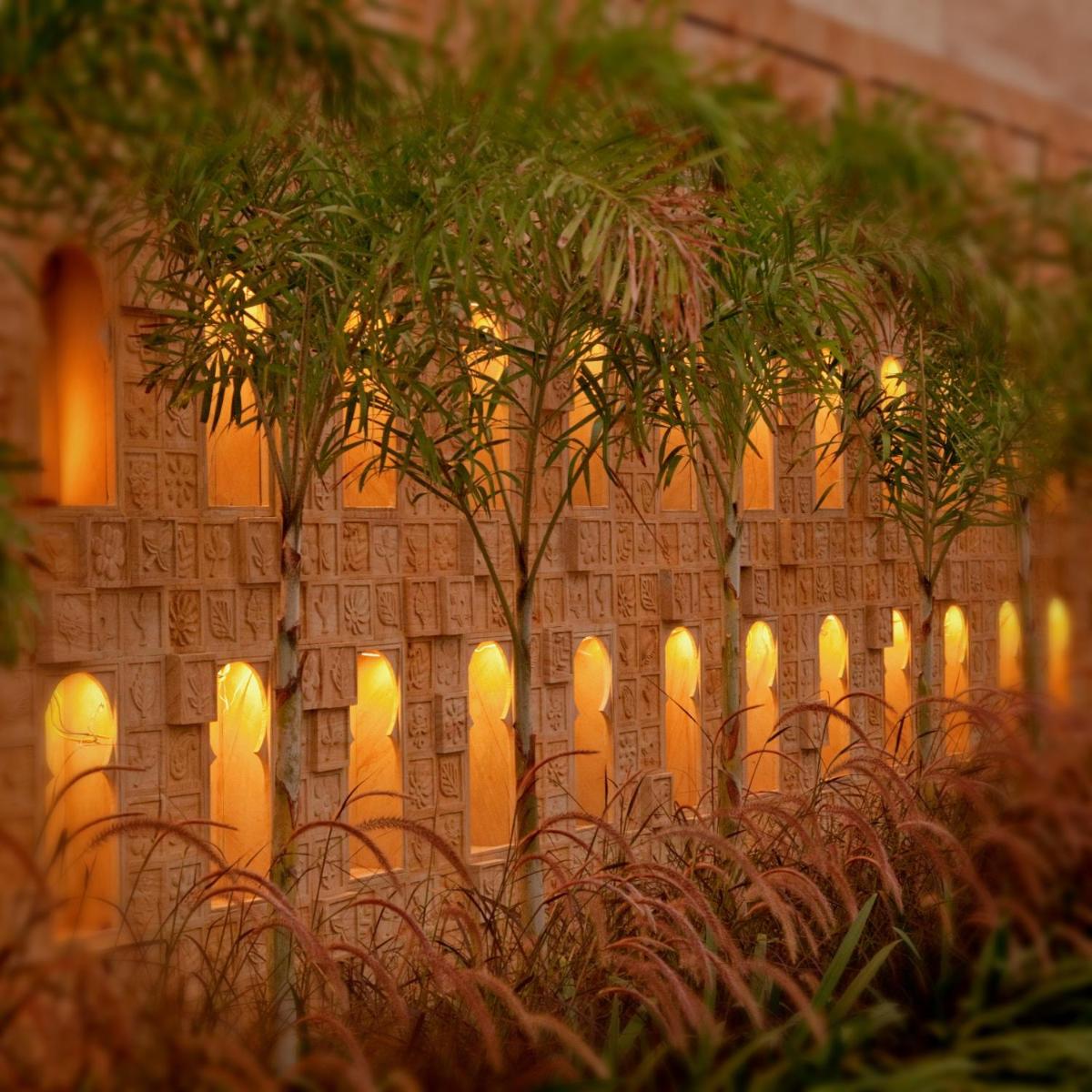 a stone wall with trees in front of a building at The Leela Palace Chennai in Chennai a stone wall with trees in front of a building at The Leela Palace Chennai in Chennai
