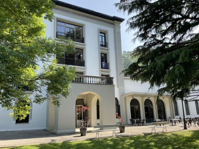 Un gran edificio blanco con bancos delante. en Balneario de Cestona, en Zestoa